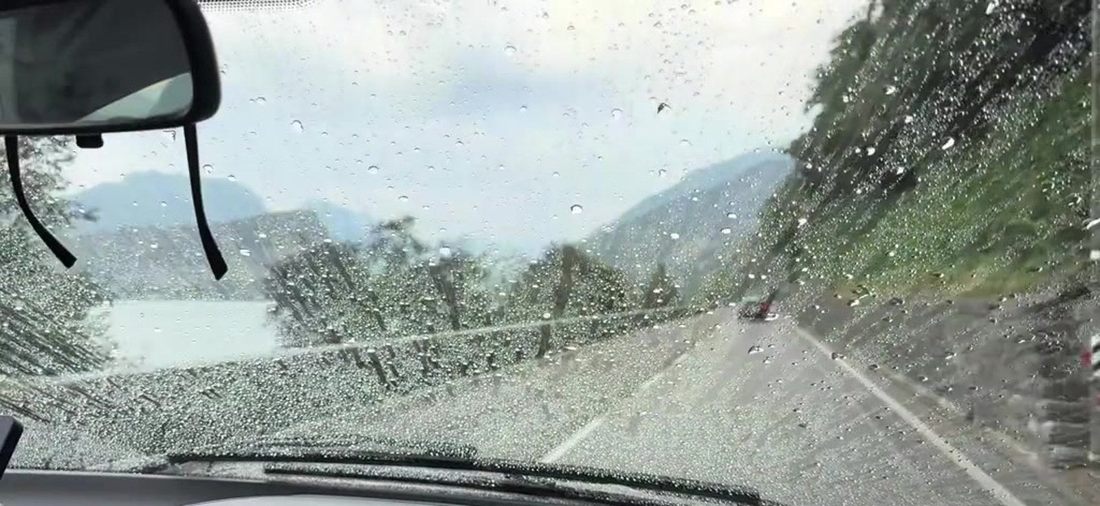 Blick durch die Windschutzscheibe im Regen – Wasser perlt ab, Scheibenwischer stehen still